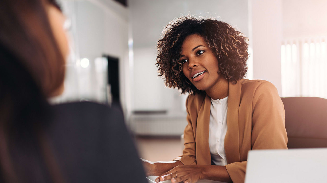 Two women talking at a desk in an office.
