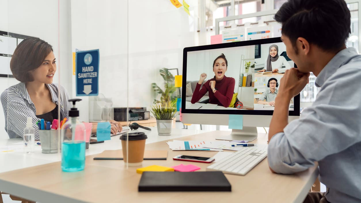 A group of people sitting at a desk and watching a video conference.