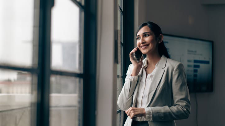 Business woman talking on the phone standing by a window.