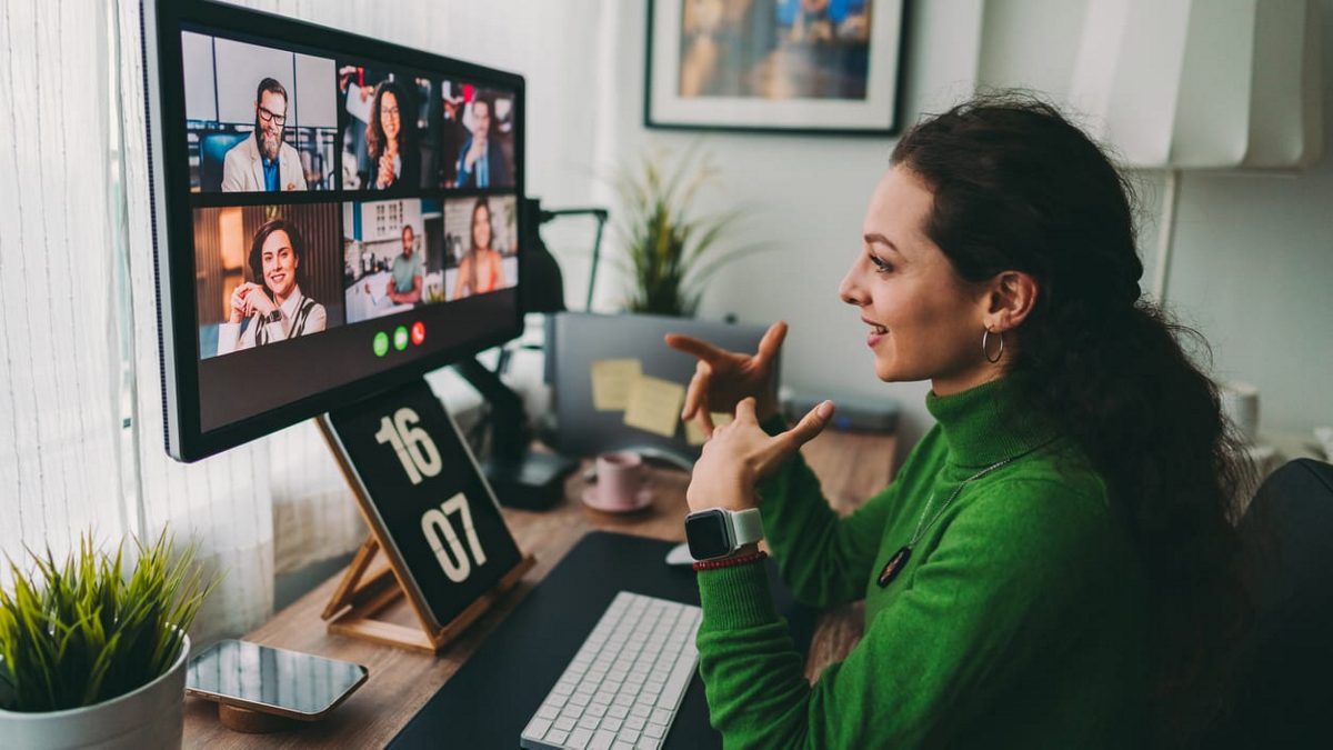 A woman in a green sweater is looking at a computer screen.