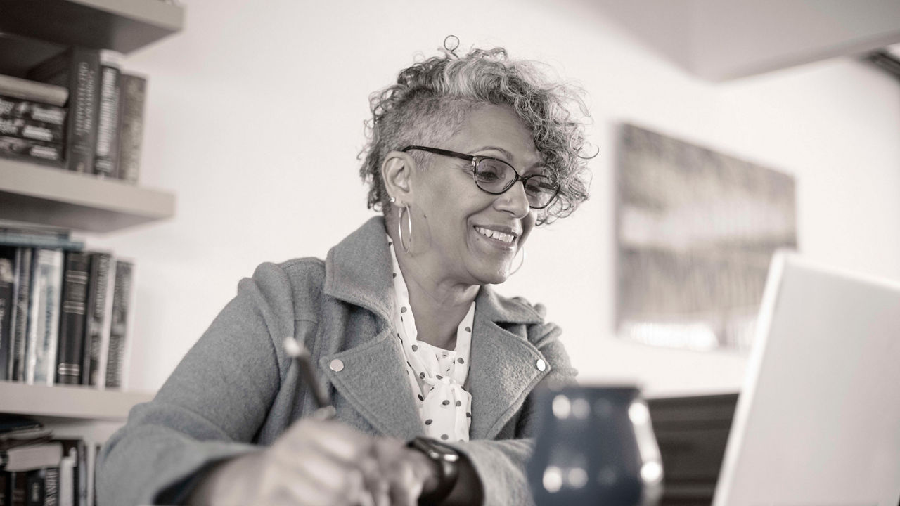A black and white photo of a woman sitting at a desk with a laptop.
