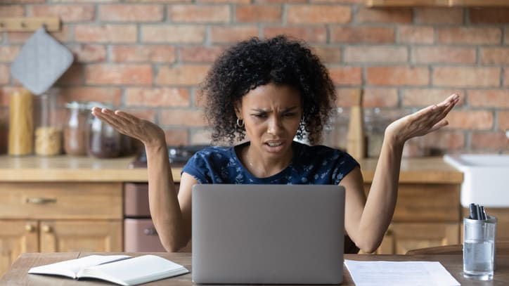 A woman is sitting at the kitchen table with a laptop.
