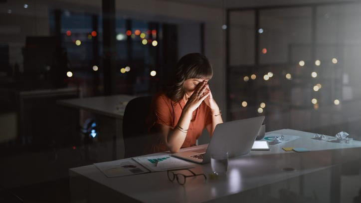 A woman sitting at a desk with a laptop at night.