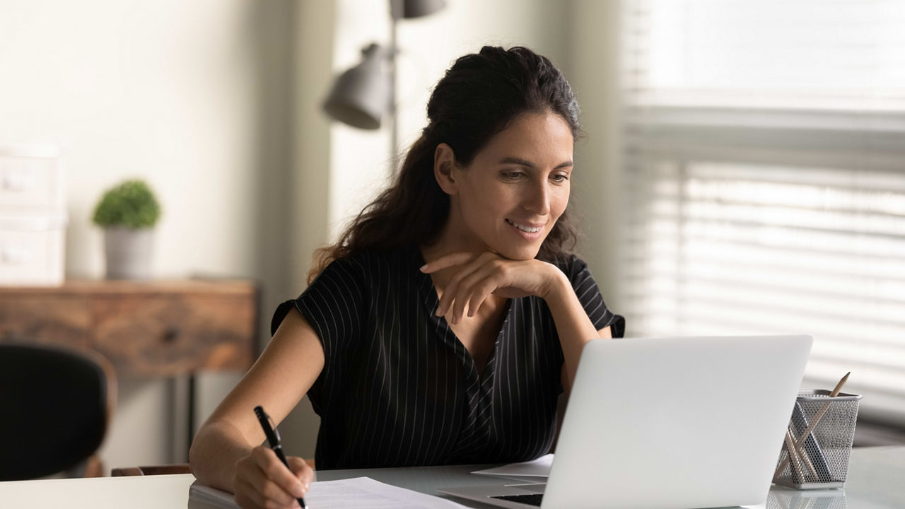 A woman sitting at a desk with a laptop and a pen.