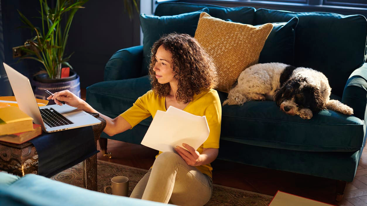 A woman sitting on a couch with a laptop and a dog.