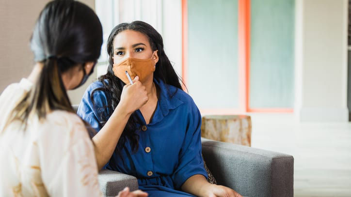 Two women sitting on a couch talking to each other.