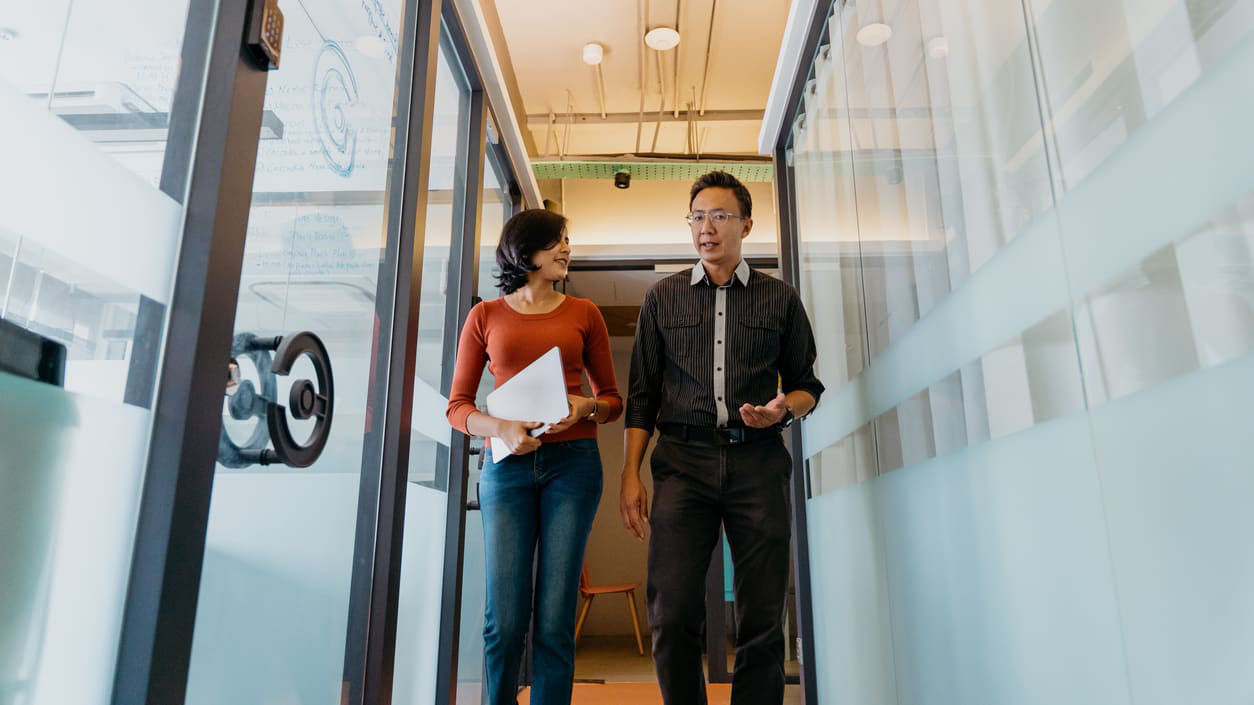 Two business people walking down a hallway in an office.