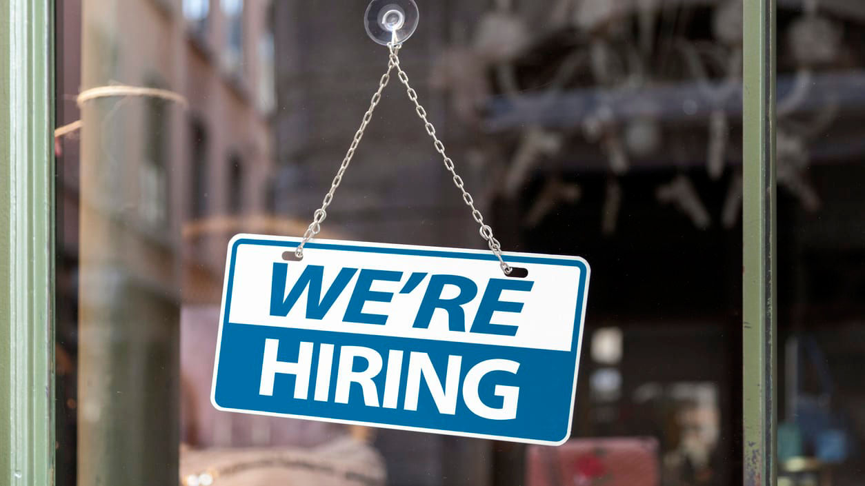 We are hiring sign hanging from a window.