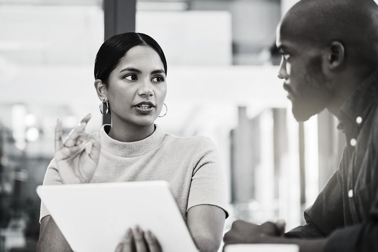 A man and a woman exchange words as he shows her the screen of a tablet.