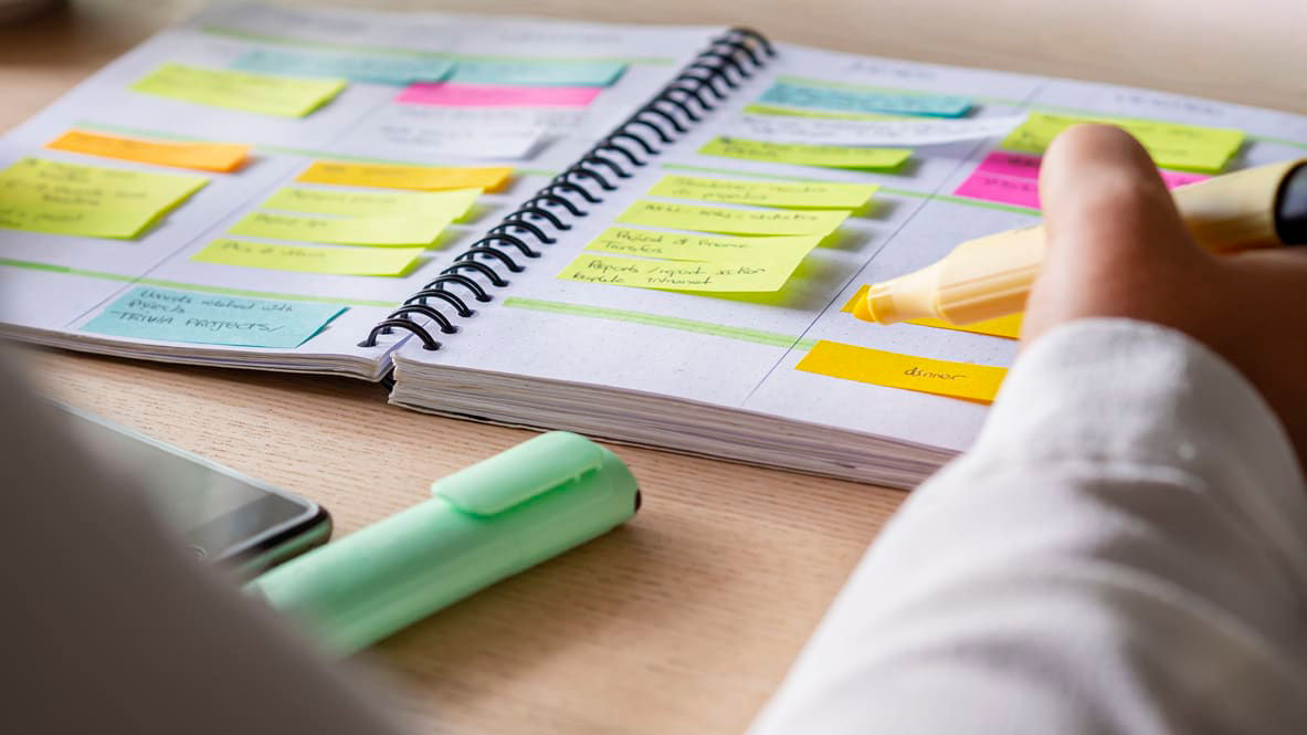 A person writing on a notebook with sticky notes.