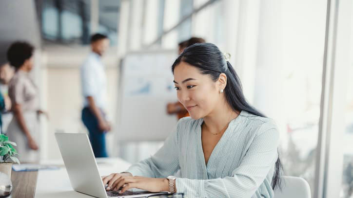 A woman is working on a laptop in an office.