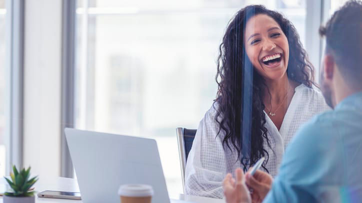 A woman and man laughing at a meeting in an office.
