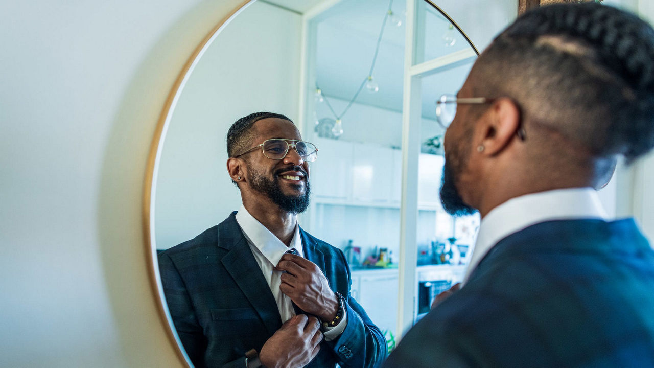 A man in a suit is adjusting his tie in front of a mirror.