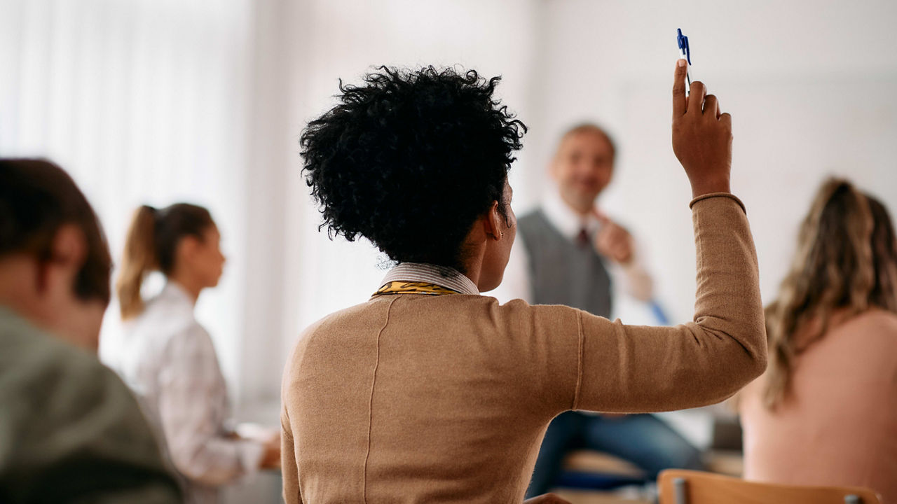 A woman in a classroom raising her hand.
