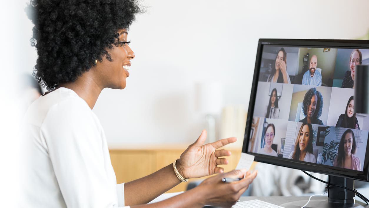 A woman in front of a computer screen showing a video conference.