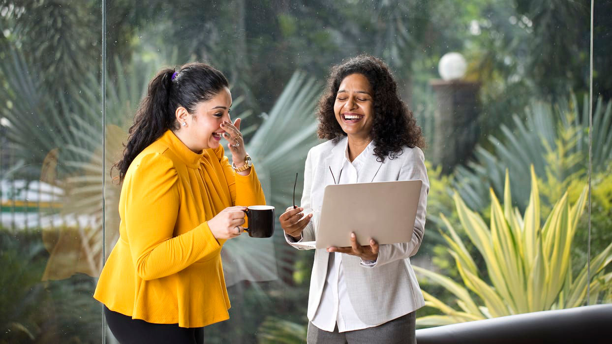 Two business women talking while holding laptops in an office.