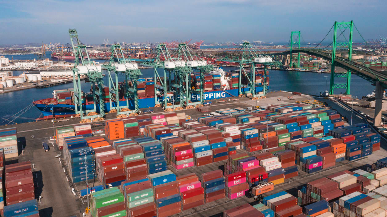 An aerial view of a container port with a bridge in the background.