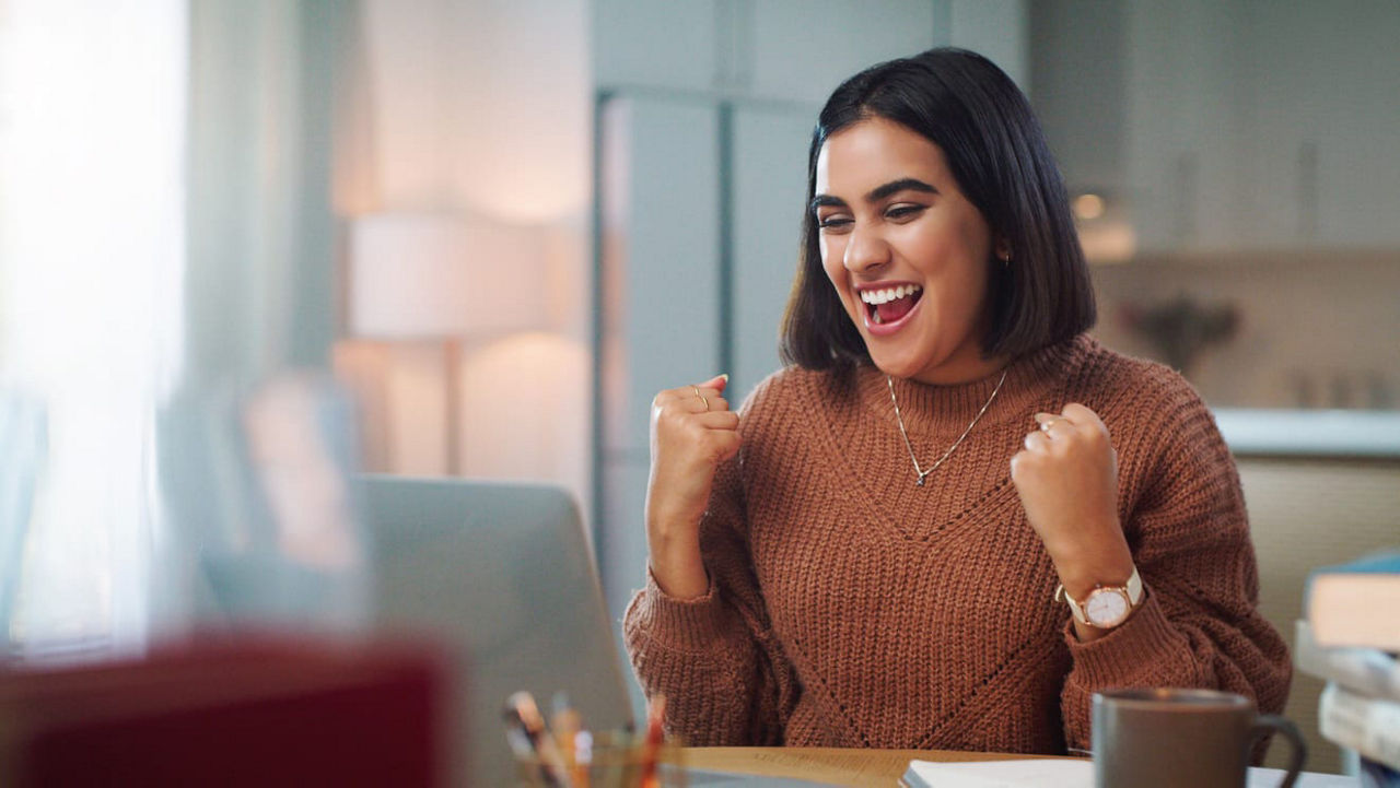 A woman is sitting at a desk with a laptop and a cup of coffee.