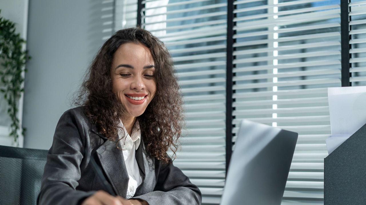 A woman in a business suit sitting at a desk with a laptop.