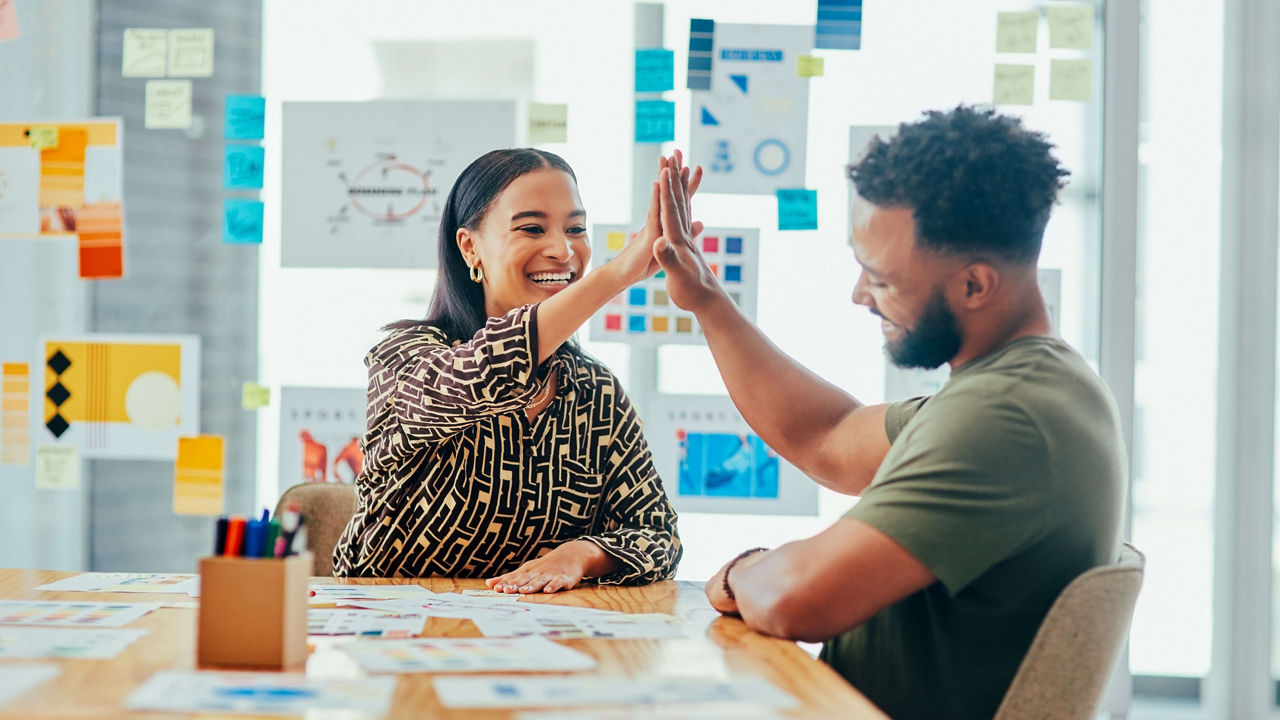 A man and woman giving each other a high five in an office.