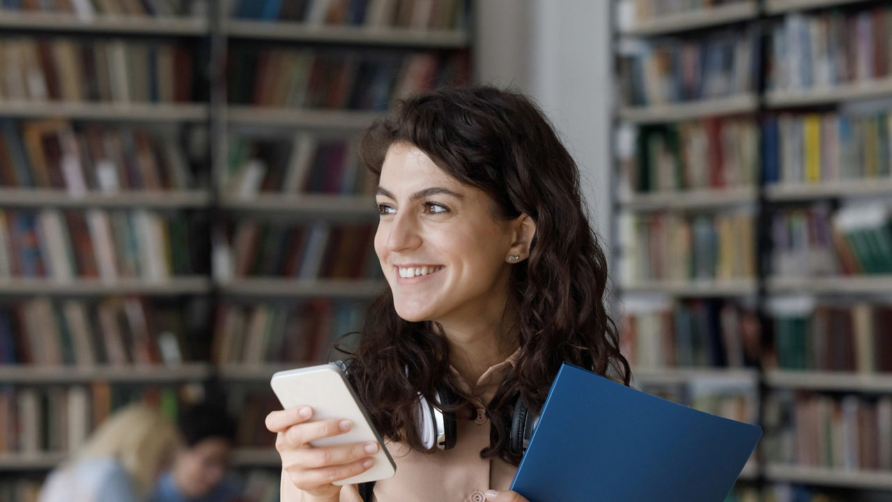 A woman holding a cell phone in a library.