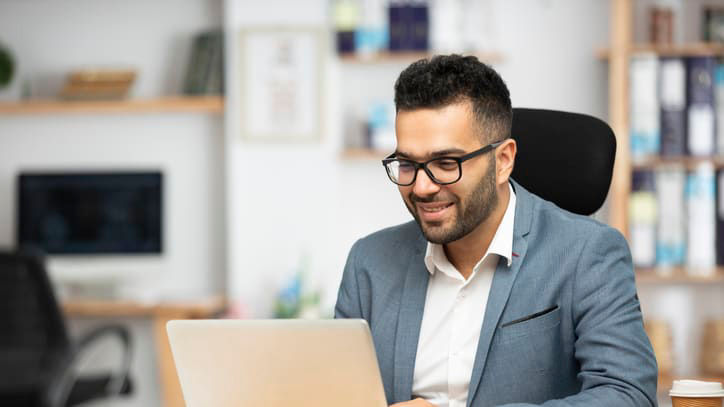 A man in glasses is using a laptop in his office.