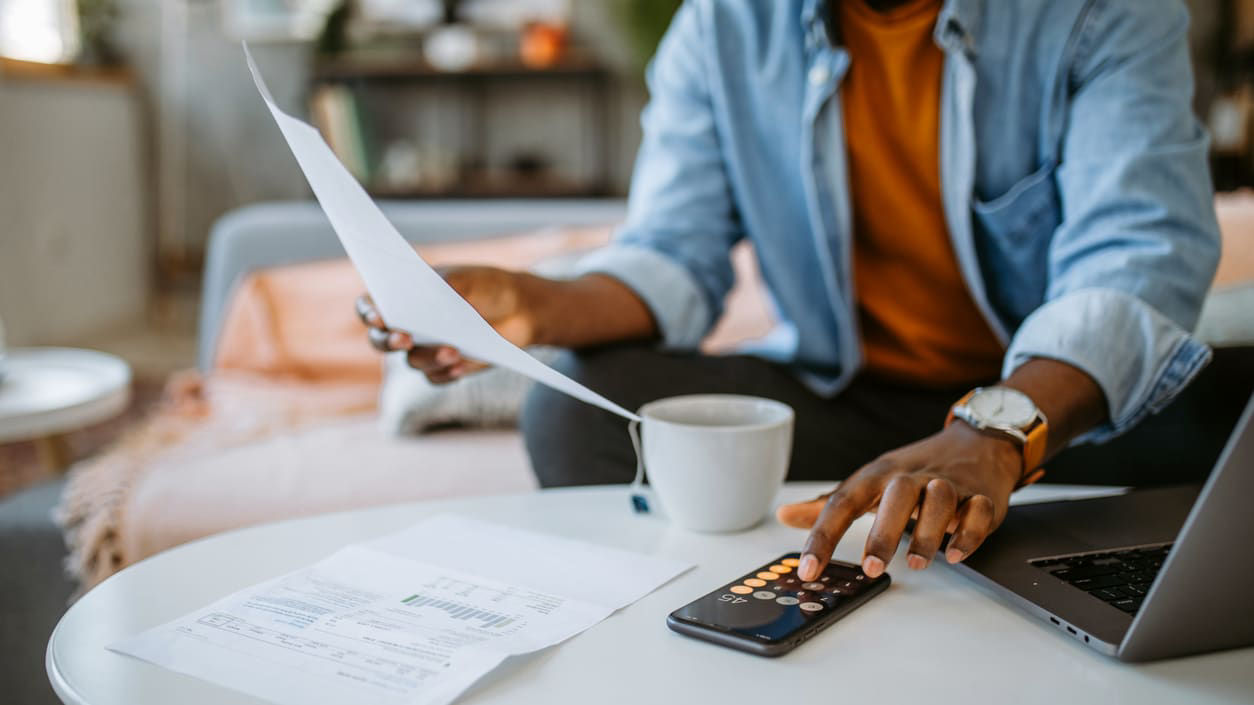 A man is working on his laptop while holding a cup of coffee.