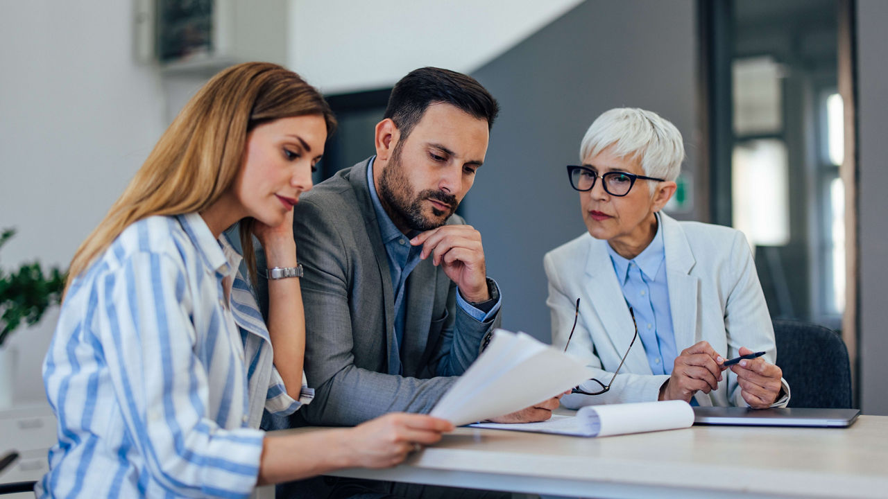 Three business people sitting at a table and looking at papers.