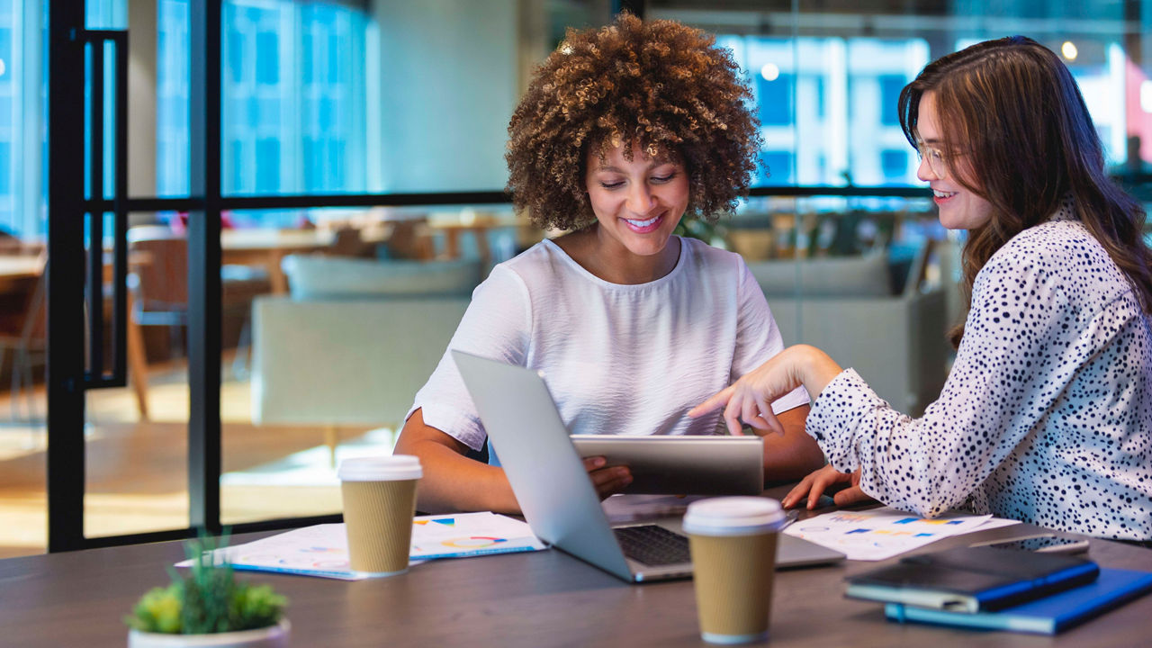 Two women sitting at a table looking at a laptop.