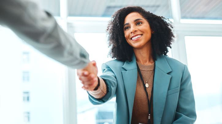 A business woman shaking hands with another woman in an office.