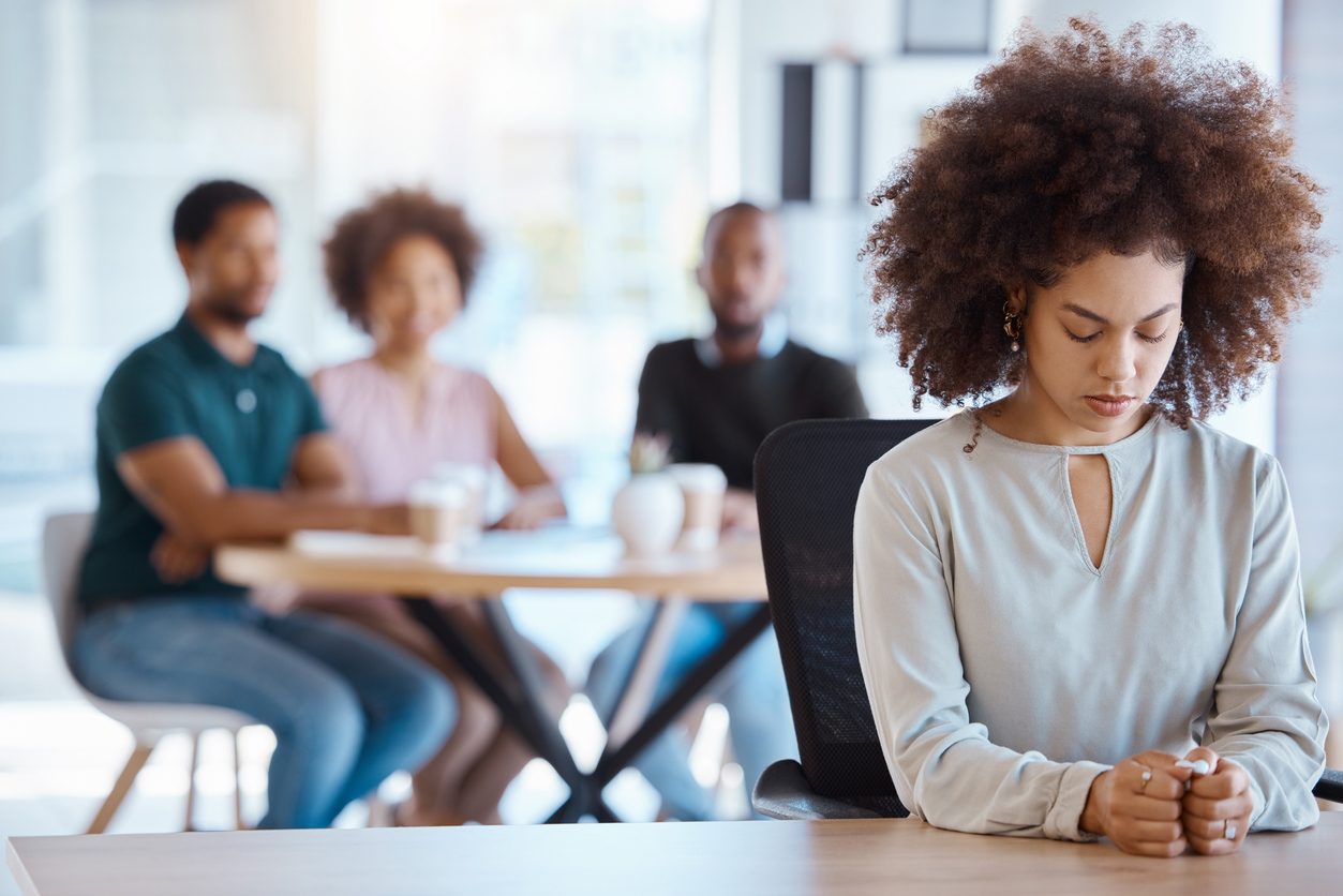 woman of color silently hears coworkers gossip in distance