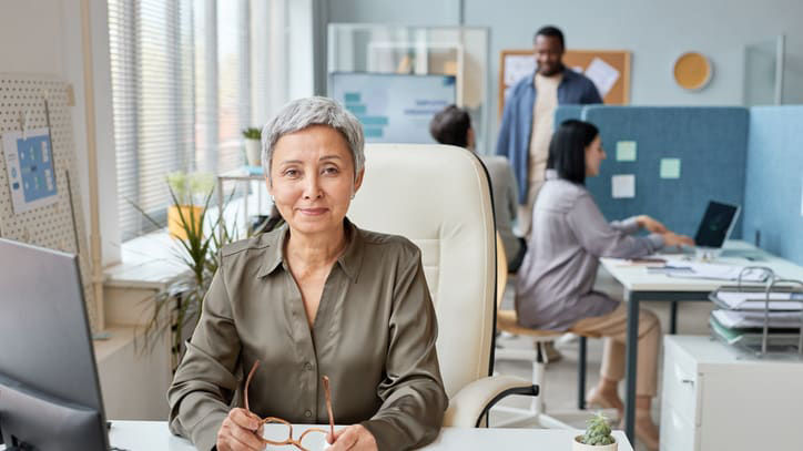 An older woman sitting at a desk in an office.