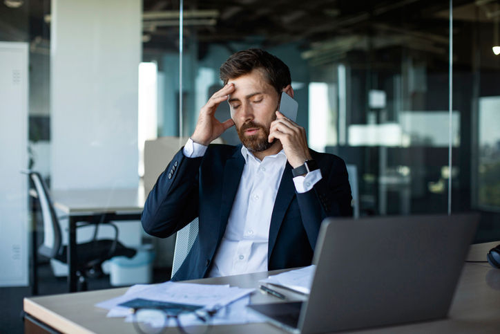 Concerned male entrepreneur talking on cellphone and touching head in stress, worried middle aged businessman suffering problems with work, having unpleasant mobile call