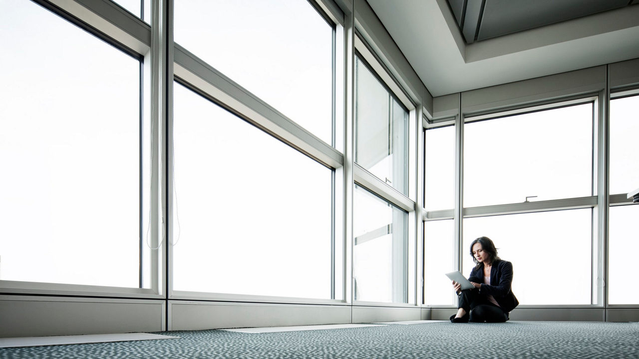 A business woman sitting on the floor in front of a large window.
