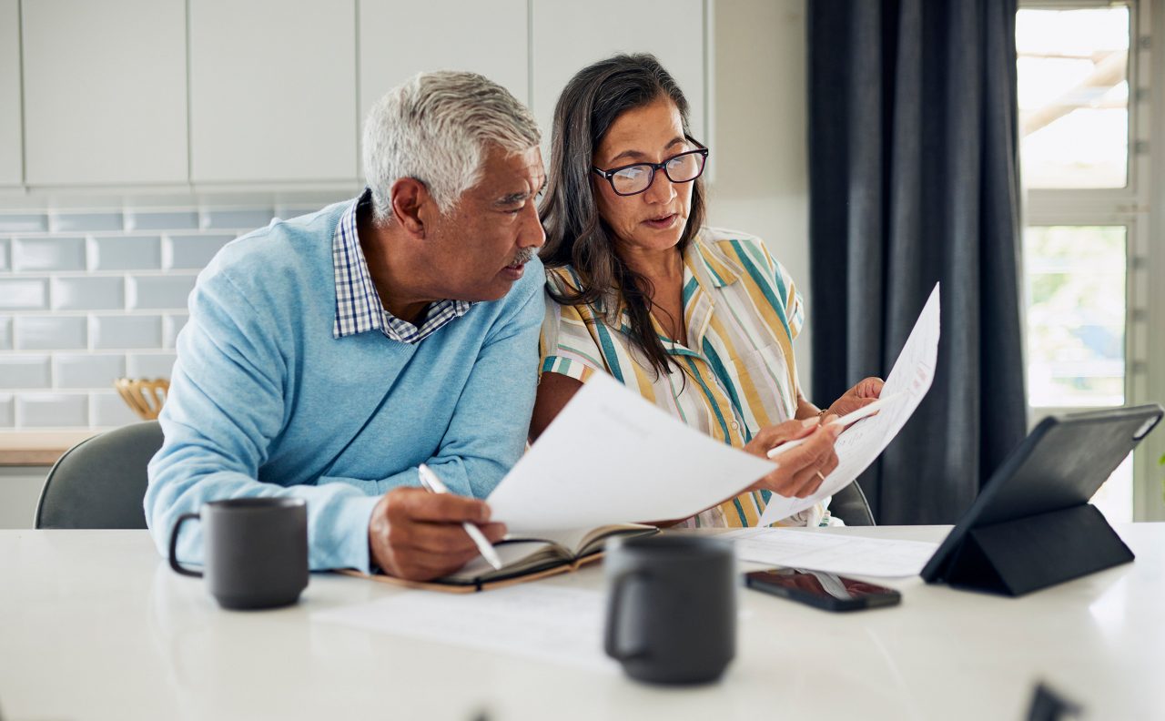 An older couple is sitting at their kitchen table reviewing financial documents.