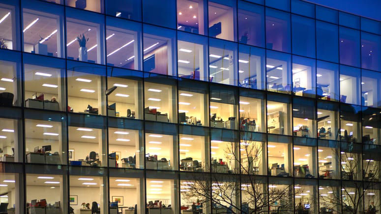 A large glass office building at night with people inside.
