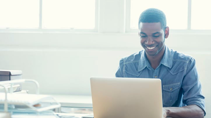 A smiling man using a laptop in his office.