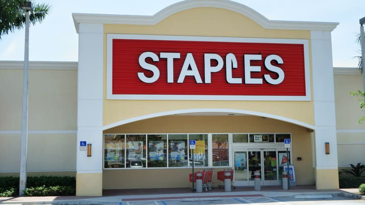 A staples store with cars parked in front of it.