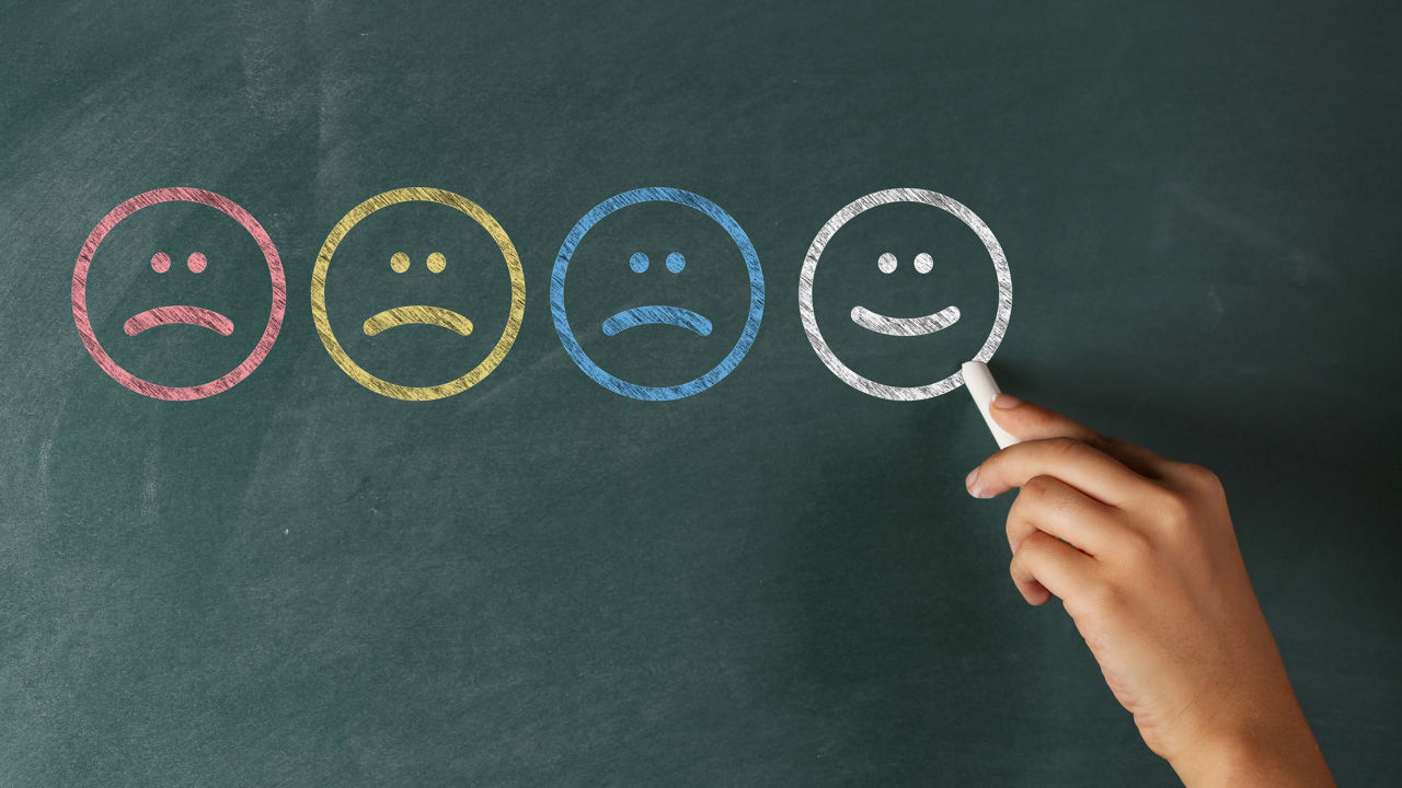 A hand drawing a smiley face on a blackboard.