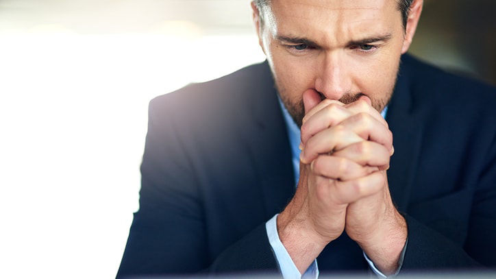 A businessman in a suit is holding his hands up in front of a laptop.