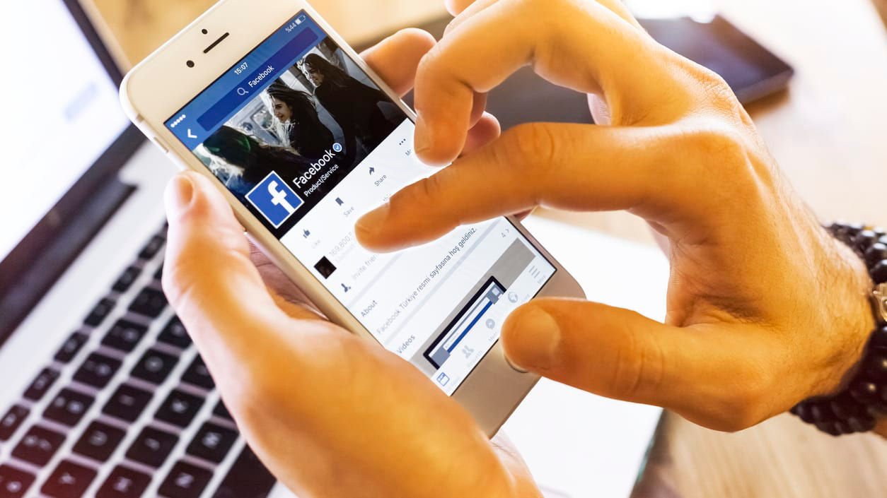 A person holding a cell phone with facebook on it.