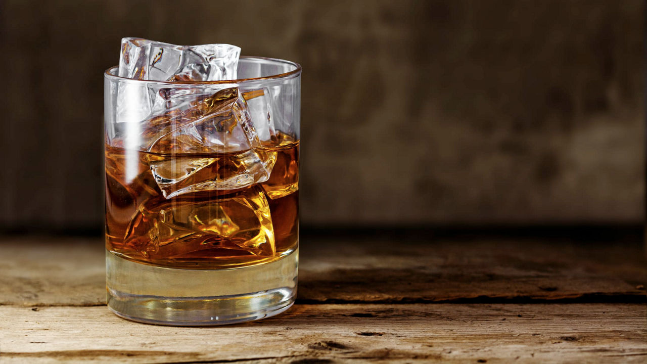 A glass of whiskey with ice cubes sitting on a wooden table.