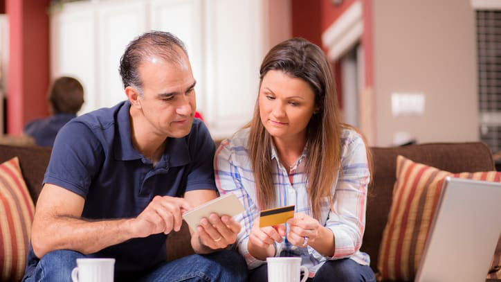 A man and woman using a credit card on a couch.