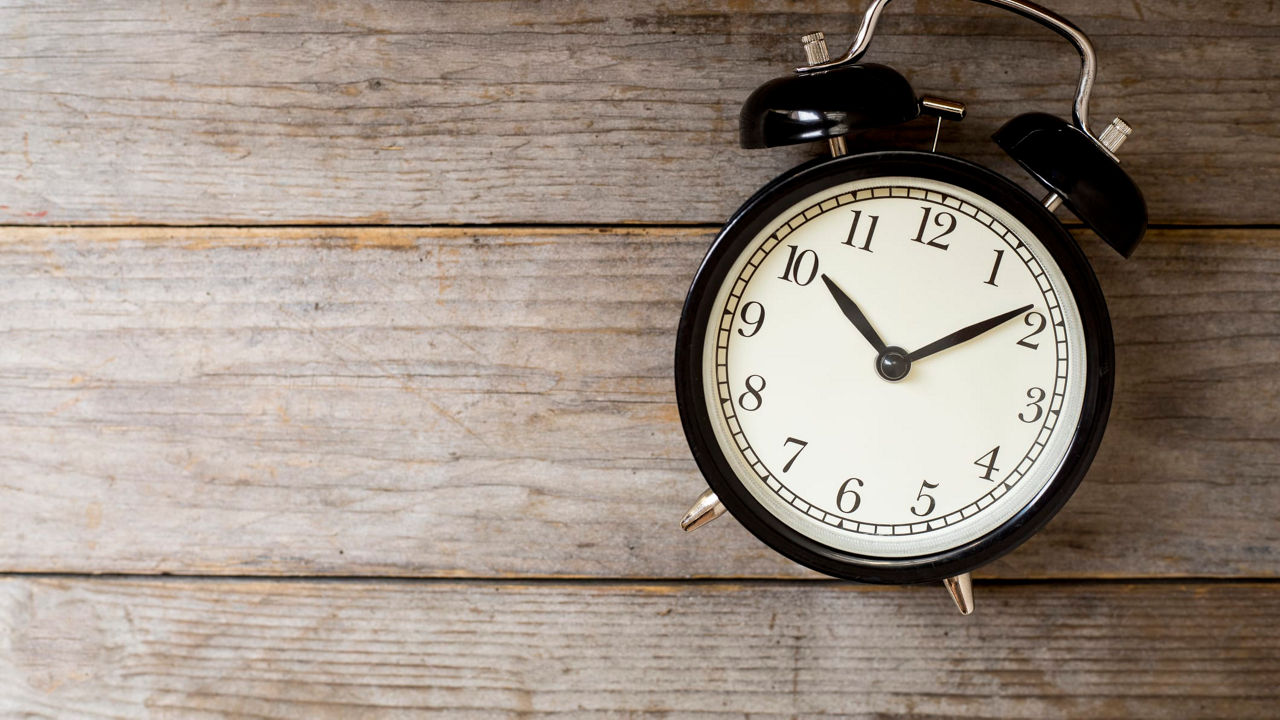 A black alarm clock on a wooden background.