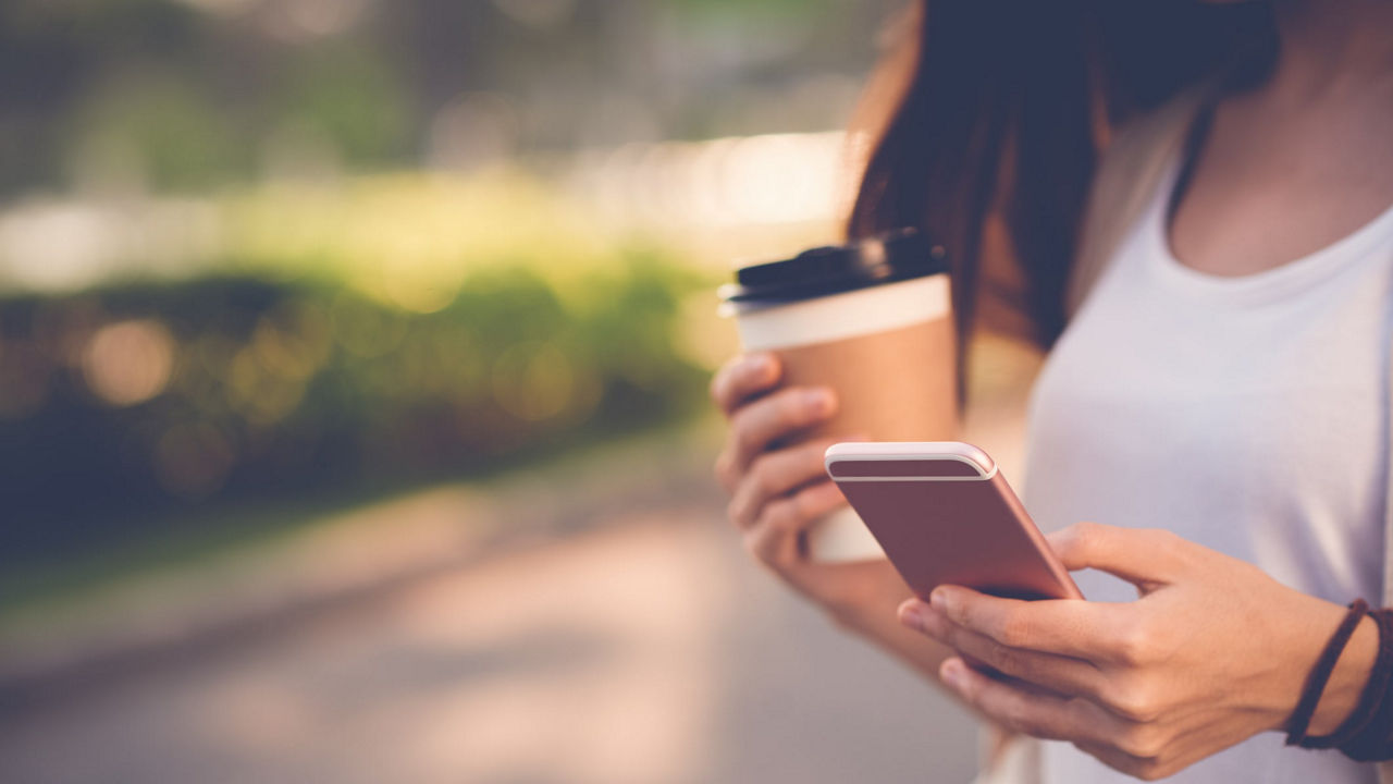 A woman holding a cup of coffee and a cell phone.