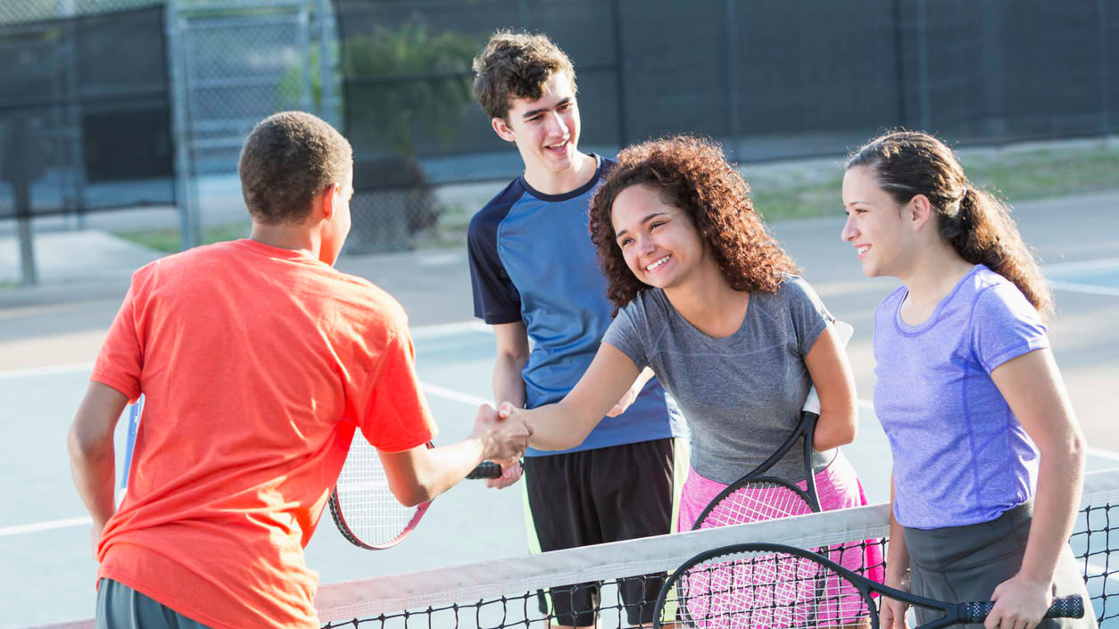 A group of young people shaking hands on a tennis court.