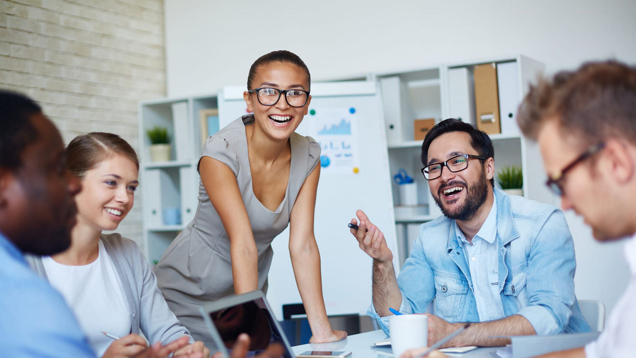 A group of people laughing around a table in an office.