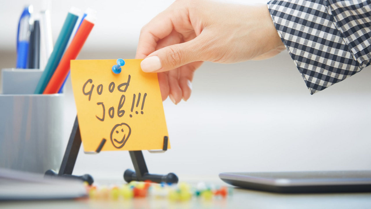 A hand holding a sticky note with the word good job on it.