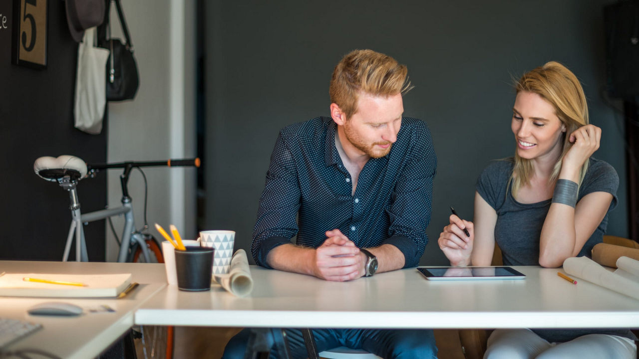 A man and woman sitting at a table looking at a tablet.