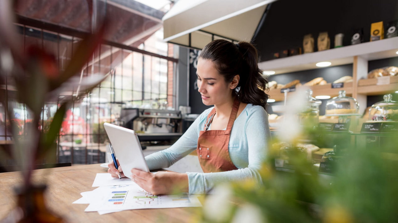 A woman in a apron working on a tablet in a coffee shop.